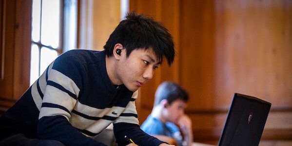 A student in a striped sweater uses a laptop.