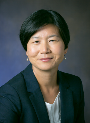 A photo of Dr. Soo Ah Kwon. She is smiling at the camera. Her hair is short, and she wears a dark suit.