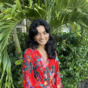 A photo of Shivani. She is smiling at the camera, has long, dark hair, and is wearing a red shirt.